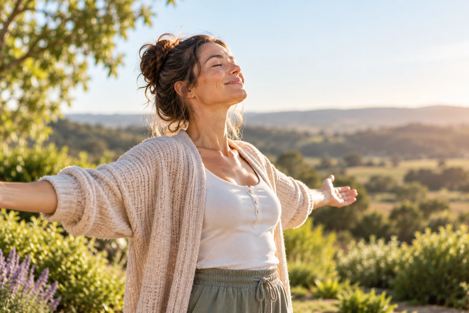A woman with arms outstretched, enjoying the sunshine over rolling countryside